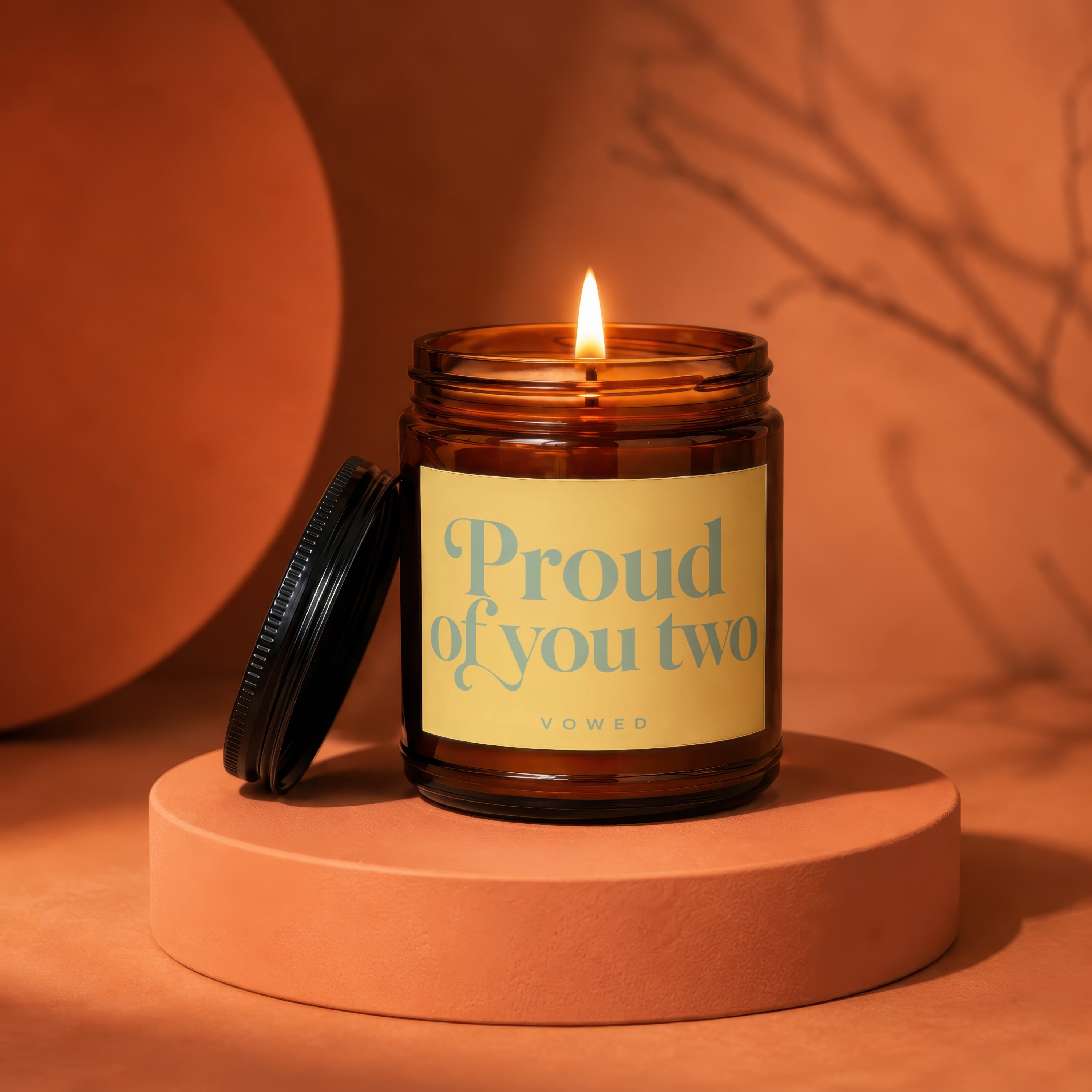 Amber jar candle with lit wick, labeled "Proud of you two".