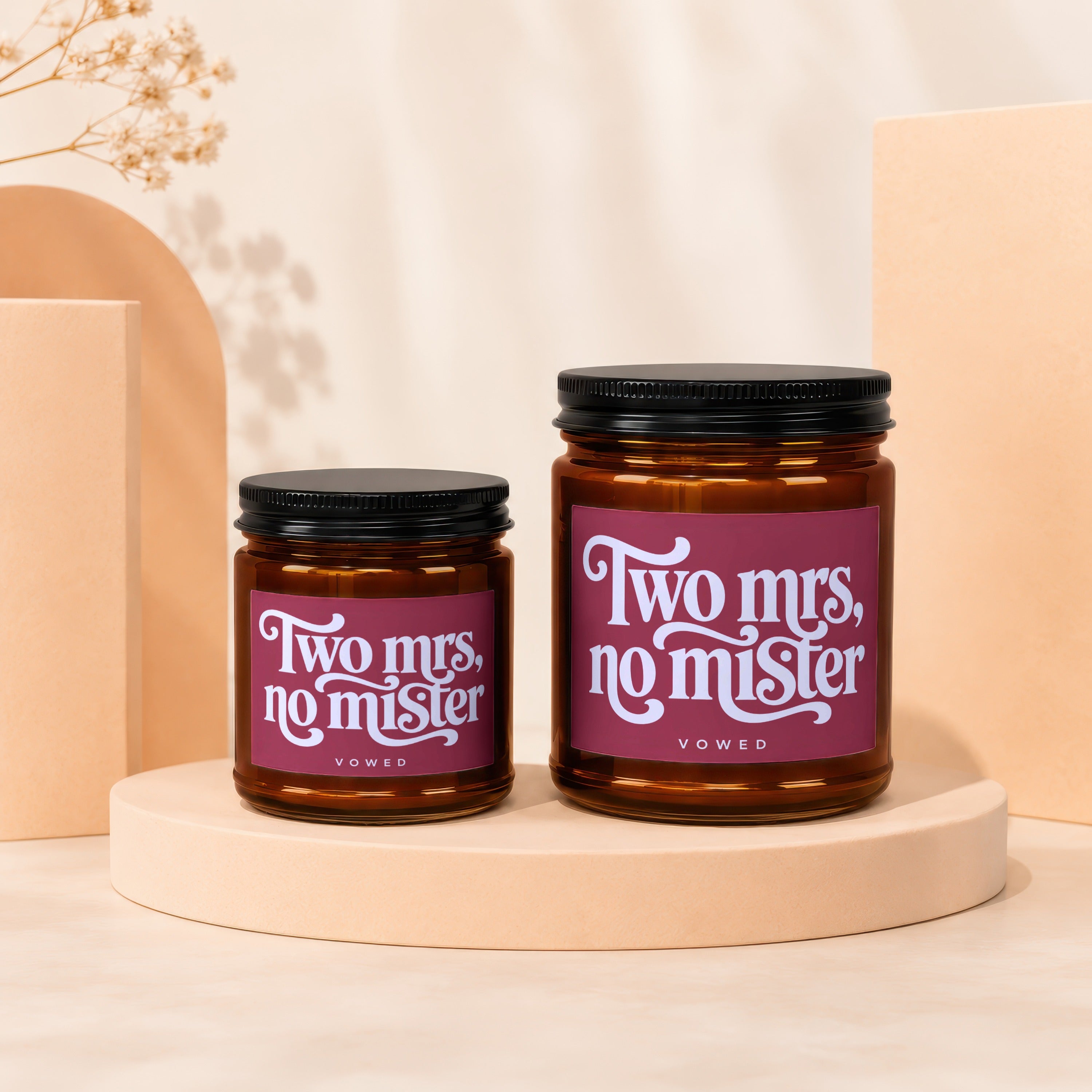 Two amber glass candles with "Two mrs, no mister" labels on a peach platform.