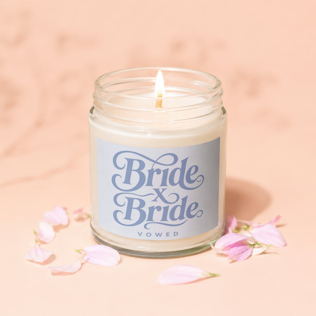 Lit candle in glass jar with "Bride x Bride Vowed" label and pink petals.