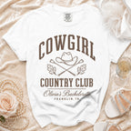 A white t-shirt featuring brown text that reads COWGIRL COUNTRY CLUB, Olivia's Bachelorette, FRANKLIN, TN.