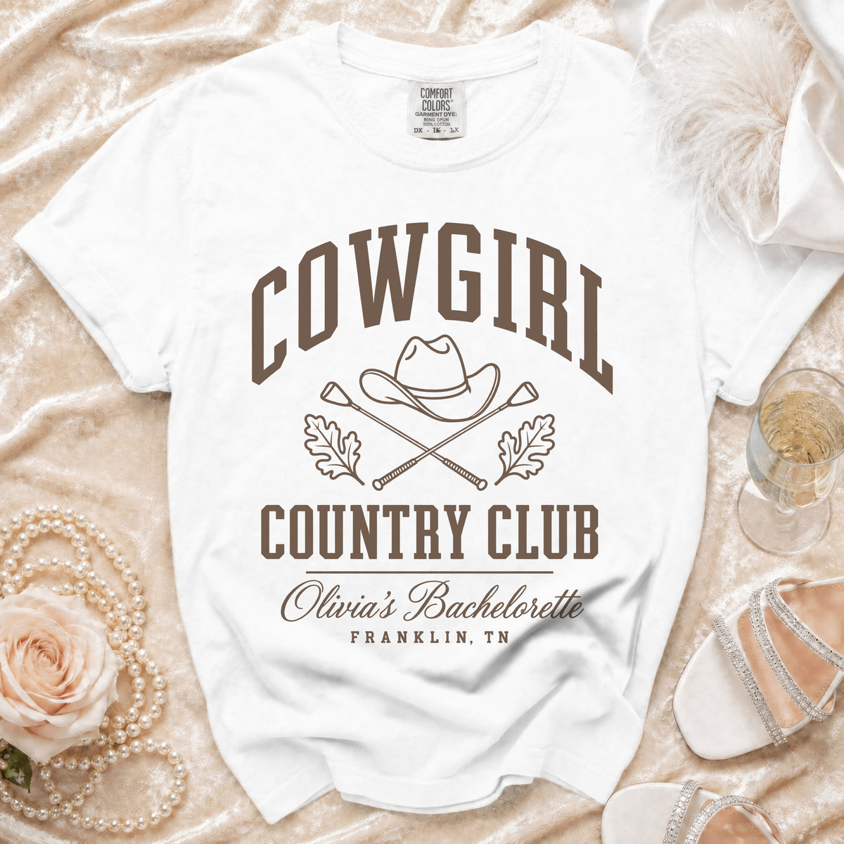 A white t-shirt featuring brown text that reads COWGIRL COUNTRY CLUB, Olivia's Bachelorette, FRANKLIN, TN.