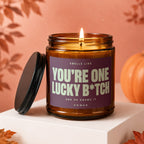 Amber glass candle with lid off, reads "You're One Lucky B*tch"