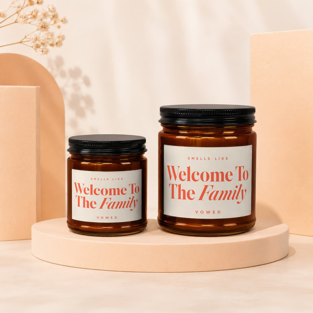 Two amber glass candles with white labels reading "Welcome To The Family" and "Vowed".