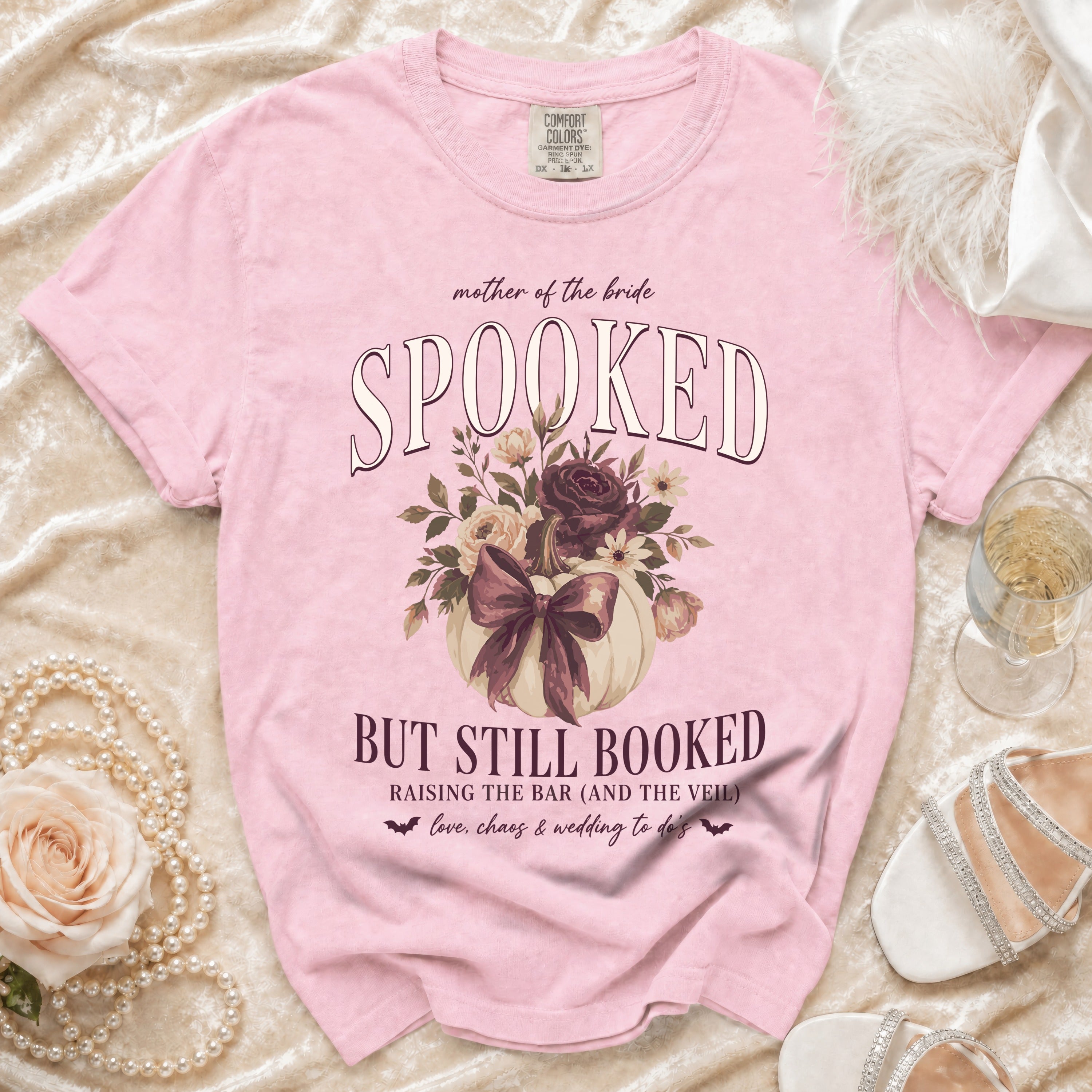 Pink t-shirt with "Mother of the Bride Spooked But Still Booked" text and floral pumpkin graphic.