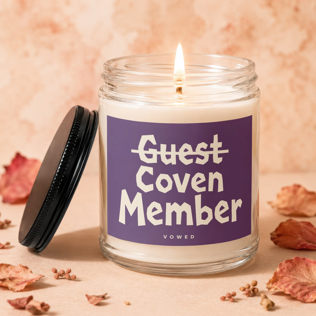 Glass candle with purple label reading "Guest Coven Member" on a peach background.