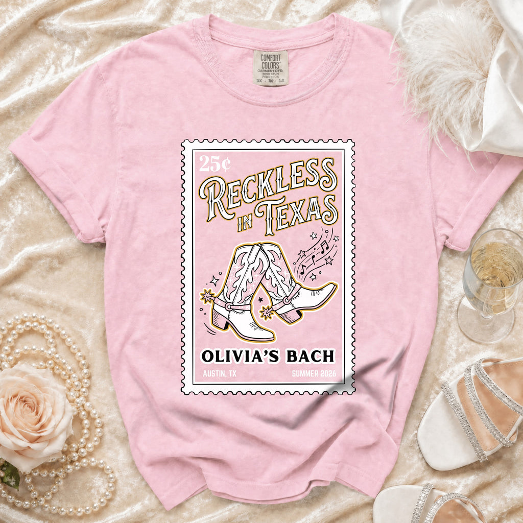 Pink t-shirt with "Reckless in Texas" and cowboy boots graphic.