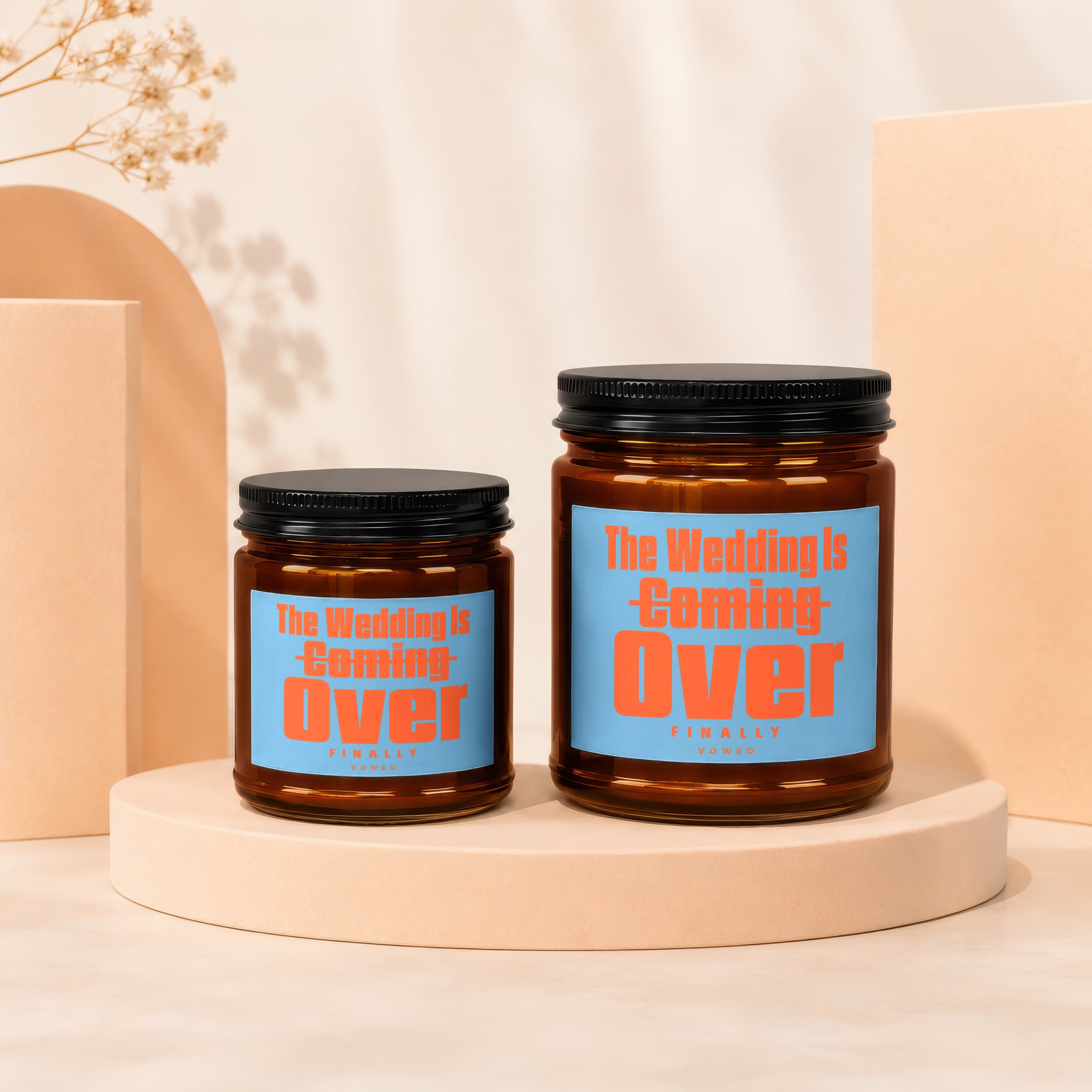 Two amber glass candles with blue labels reading "The Wedding is Coming Over" in orange.
