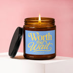 Amber candle burning with "Worth the Wait" label on pink background.