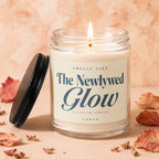 Glass jar candle with a lit wick, lid off, labeled "The Newlywed Glow".