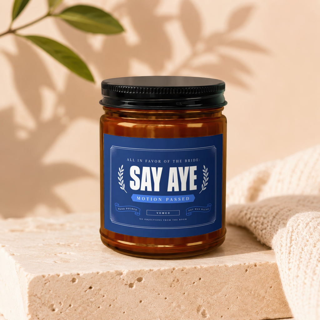 Amber jar candle with blue label reading "Say Aye, Motion Passed, Vowed"