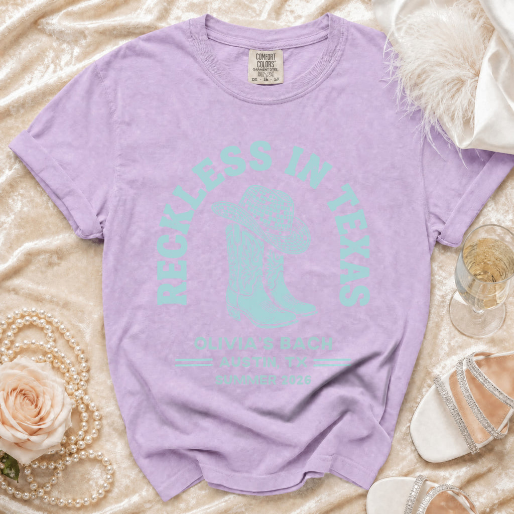 Light purple t-shirt with turquoise "Reckless in Texas" and cowboy boot graphic.