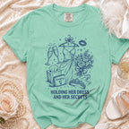 Teal Comfort Colors t-shirt with sketch of dress, champagne, and "Holding Her Dress and Her Secrets".