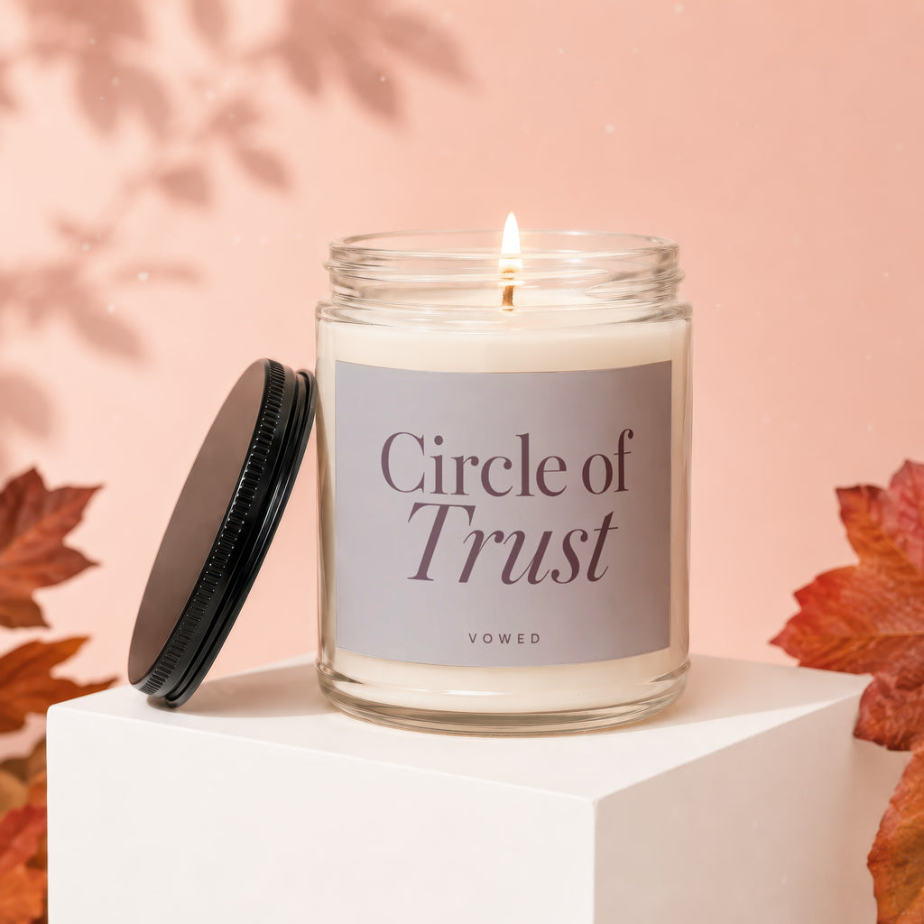 Lit glass candle with "Circle of Trust" label next to lid, autumnal leaves.