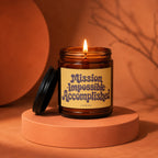 Burning brown glass candle with 'Mission Impossible Accomplished' text on label.