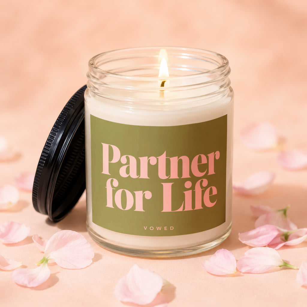 A lit candle with "Partner for Life" printed on label, surrounded by petals.