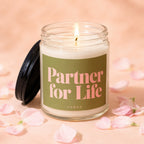 A lit candle with "Partner for Life" printed on label, surrounded by petals.