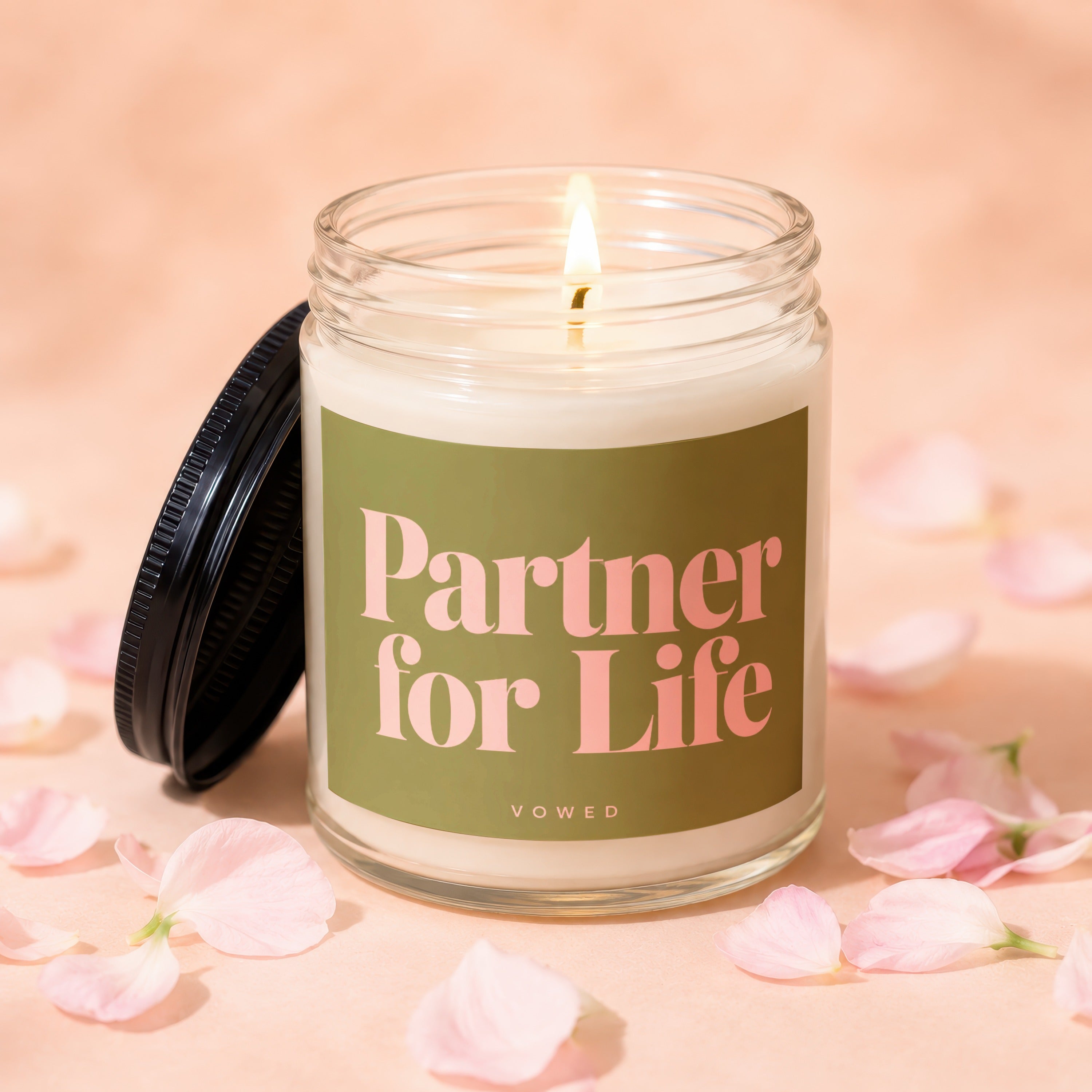 A lit candle with "Partner for Life" printed on label, surrounded by petals.