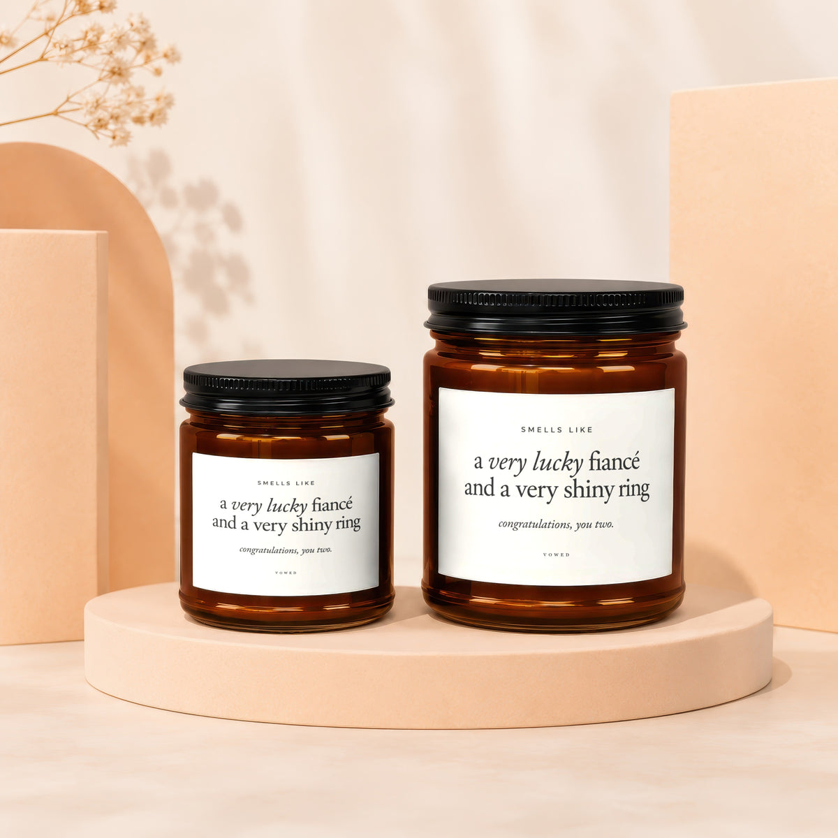 Two amber glass candles with black lids, reading "a very lucky fiancé and a very shiny ring".
