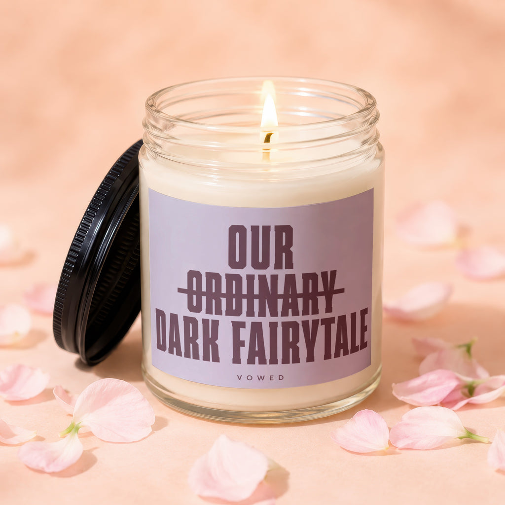 Glass candle with burning wick and lid open, showing the text "OUR ORDINARY DARK FAIRYTALE VOWED"