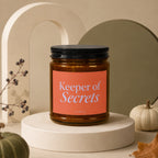 Brown glass candle with orange label that reads "Keeper of Secrets Vowed".