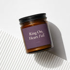 Amber jar candle with dark purple label reading "Ring On, Heart Full."