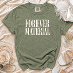 Olive green t-shirt with "FOREVER MATERIAL" text, styled with pearls and shoes.