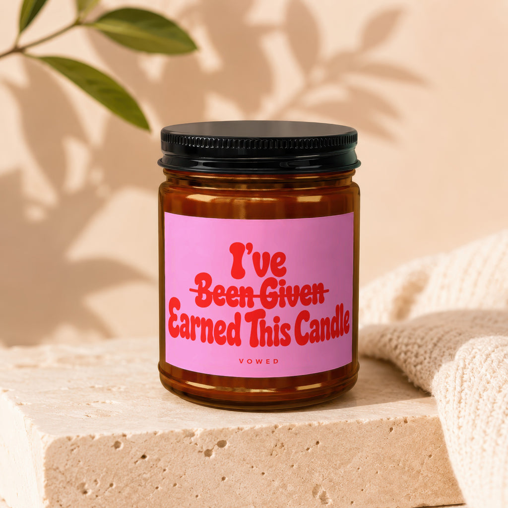 Brown glass candle with pink label reading "I've Been Given Earned This Candle. VOWED".