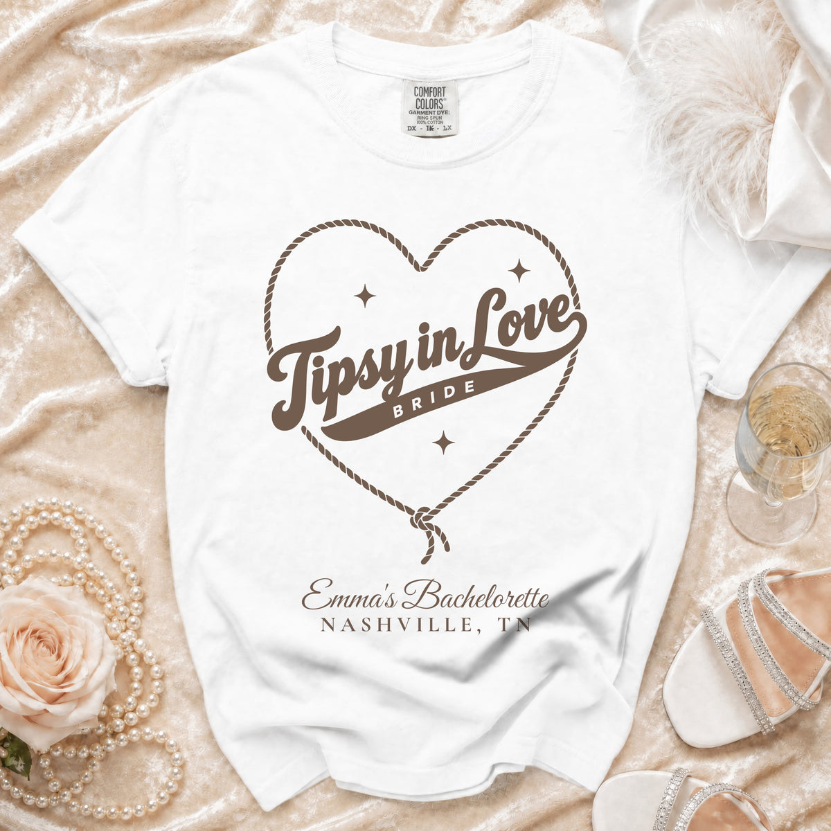 White t-shirt with brown rope heart graphic, Tipsy in Love text, and Emma's Bachelorette Nashville, TN text.