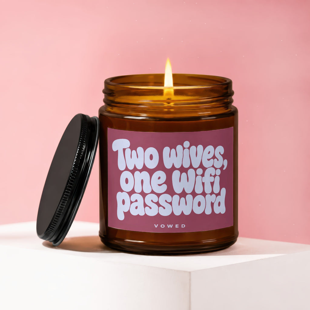 Amber jar candle with lit flame, lid removed, reading "Two wives, one wifi password."