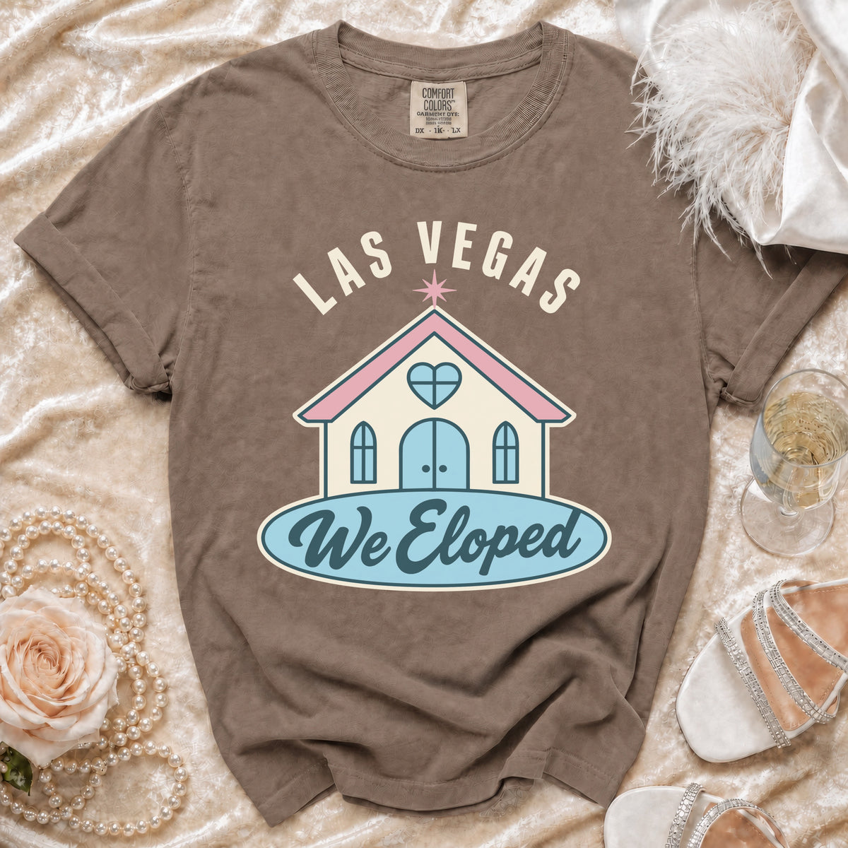 "Las Vegas We Eloped" graphic on a brown t-shirt with wedding accessories.