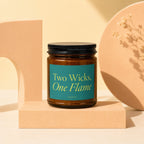 Amber candle with a teal label reading "Two Wicks, One Flame" and "vowed".