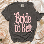 Dark grey t-shirt with pink "Bride to Be" text, ring, and floral bouquet graphic.