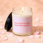 Glass candle with lit flame and pink label reading "Every Great Love Story Starts With a Question."