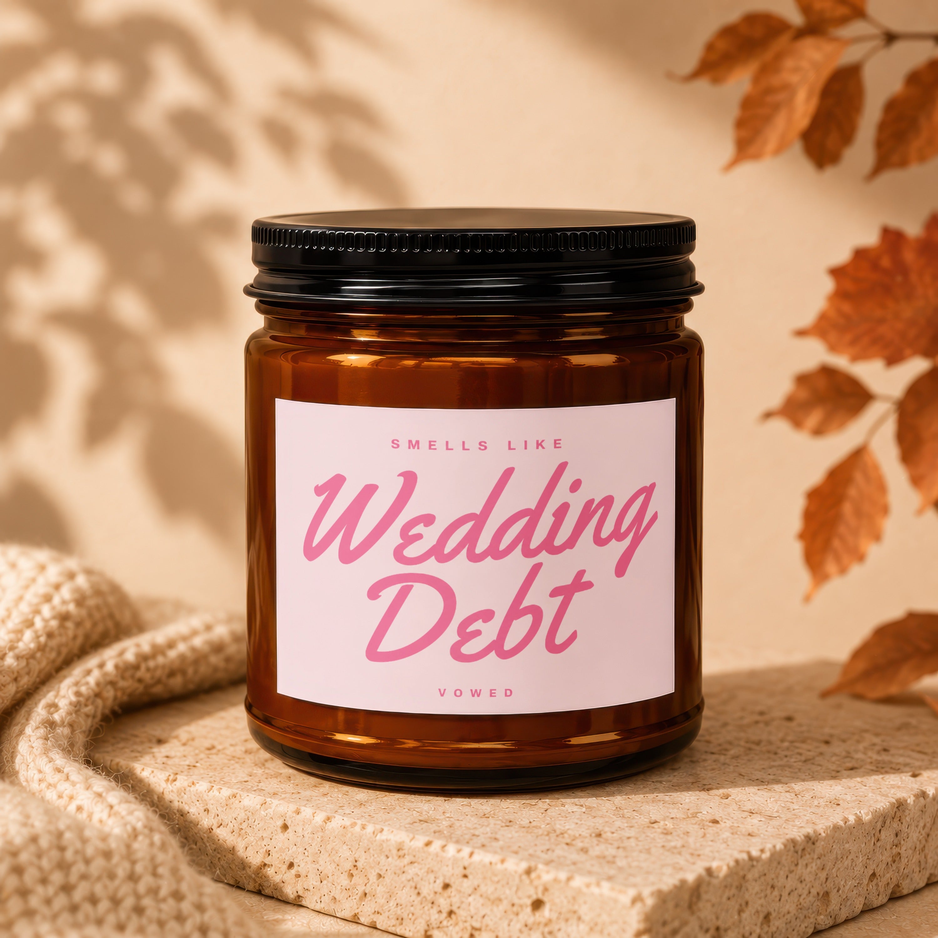Amber candle with black lid labeled "Smells Like Wedding Debt Vowed".