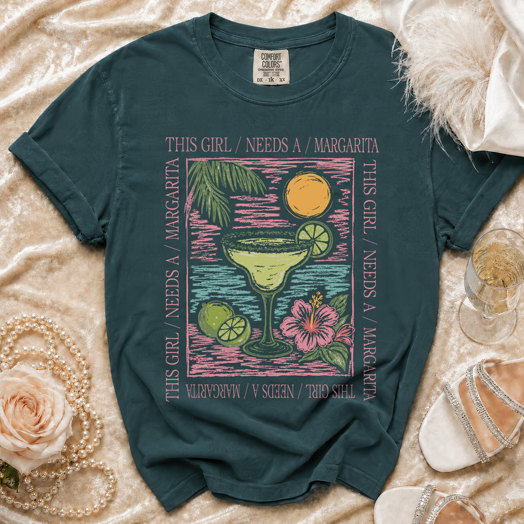 Teal t-shirt with a margarita graphic and the text "This girl needs a margarita."