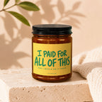 Amber jar candle with yellow label reading "I PAID FOR ALL OF THIS AND I WOULD DO IT AGAIN"