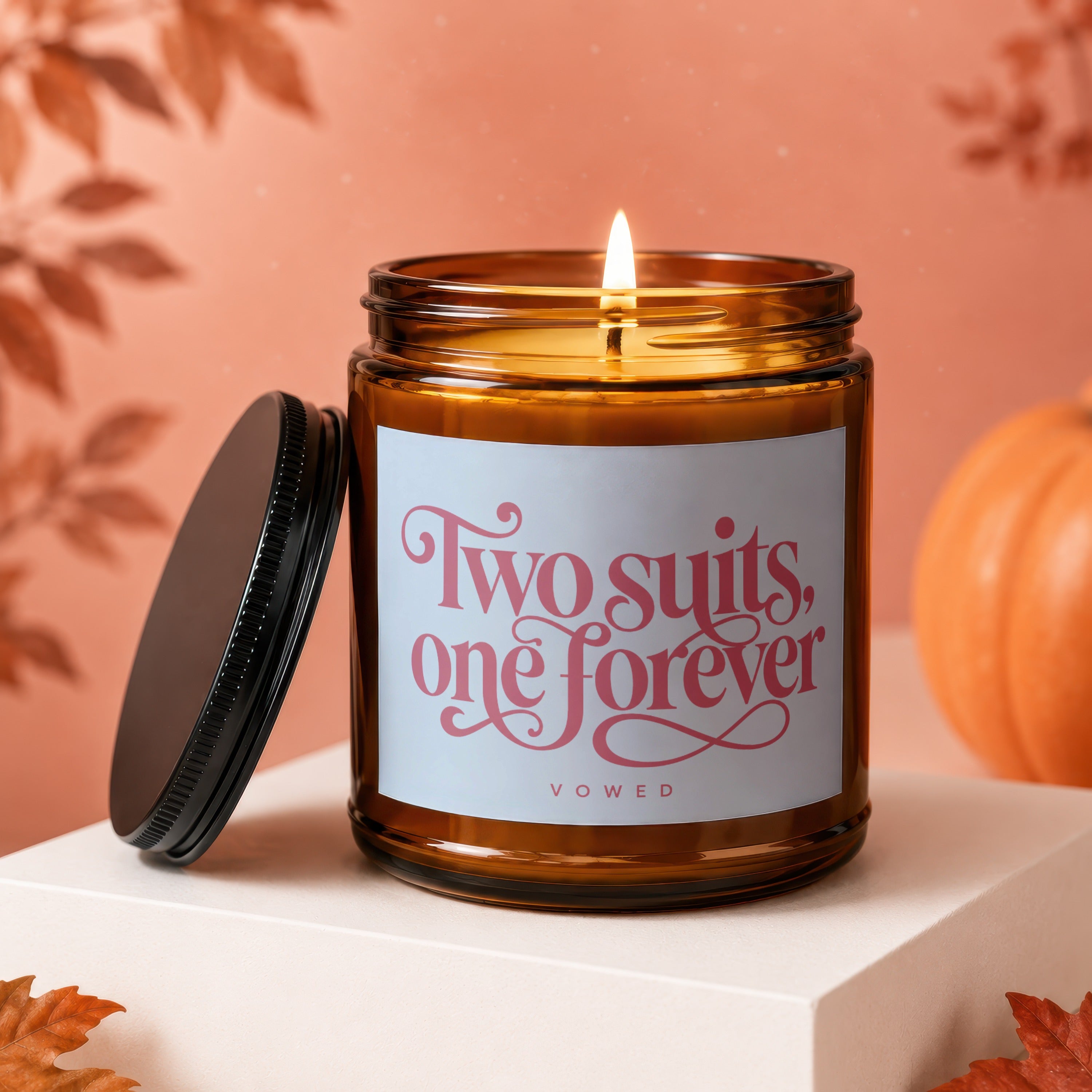 Amber candle with pink text "Two suits, one forever" and "vowed" on label.