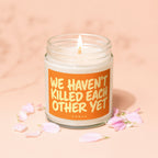 A lit jar candle with the text "WE HAVEN'T KILLED EACH OTHER YET" and "VOWED".