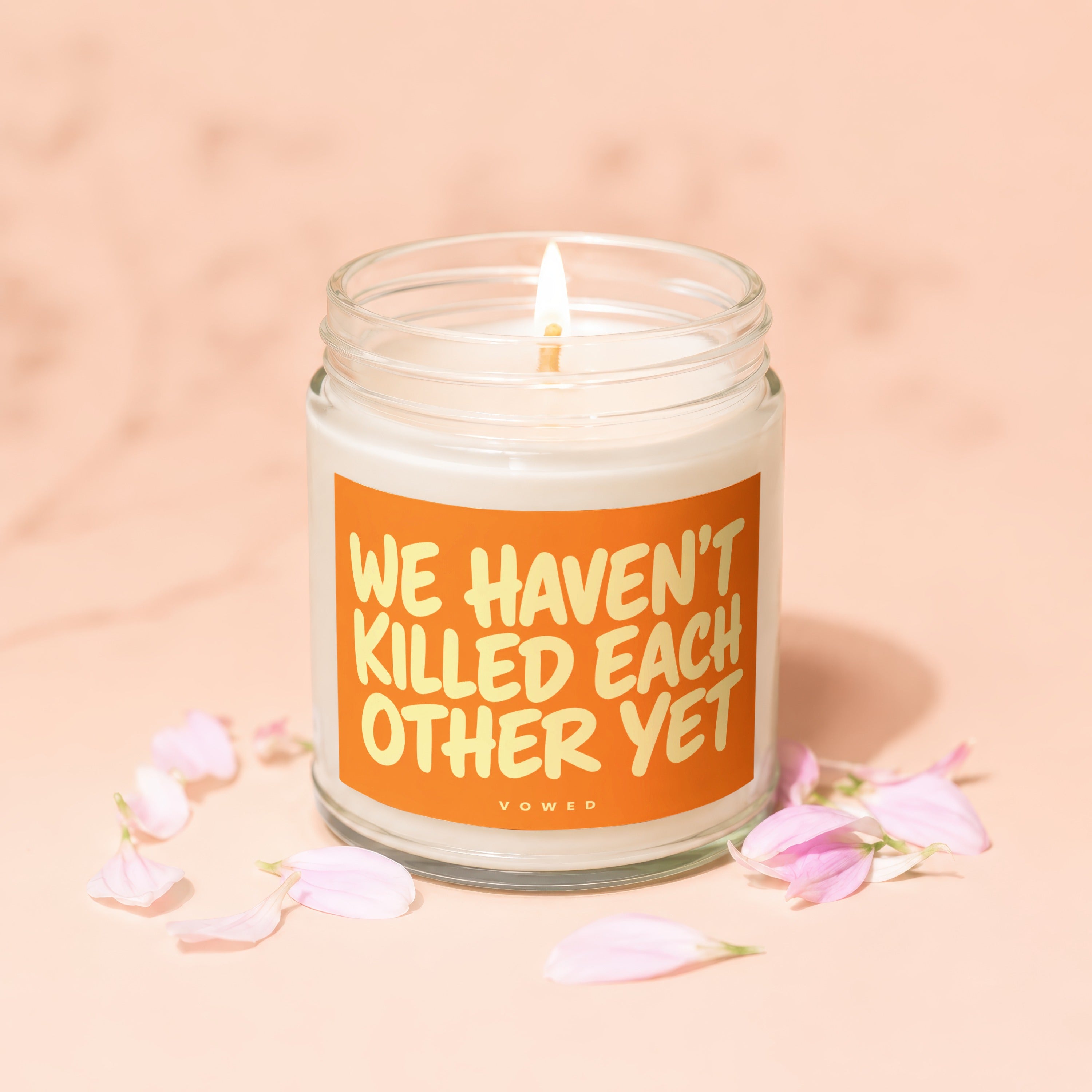 A lit jar candle with the text "WE HAVEN'T KILLED EACH OTHER YET" and "VOWED".