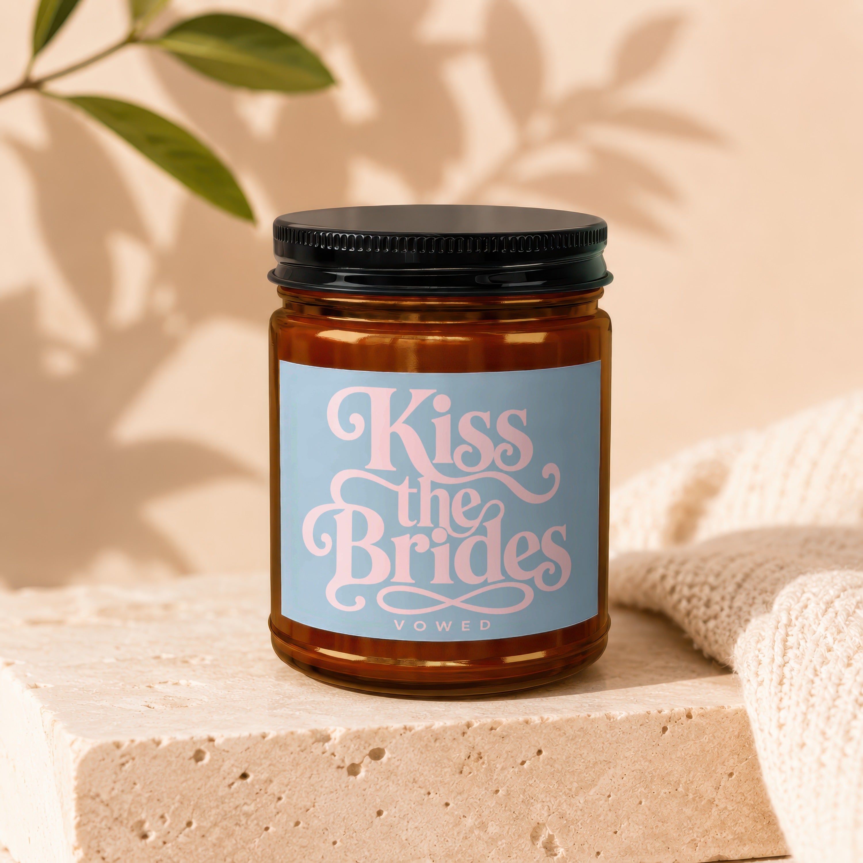 Amber jar candle with "Kiss the Brides" and "VOWED" text on blue label.