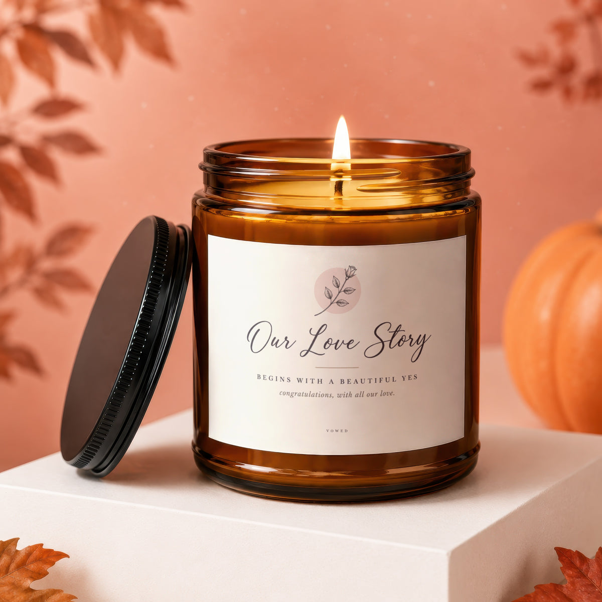 Amber jar candle with lit wick, "Our Love Story" label, and autumn decor.