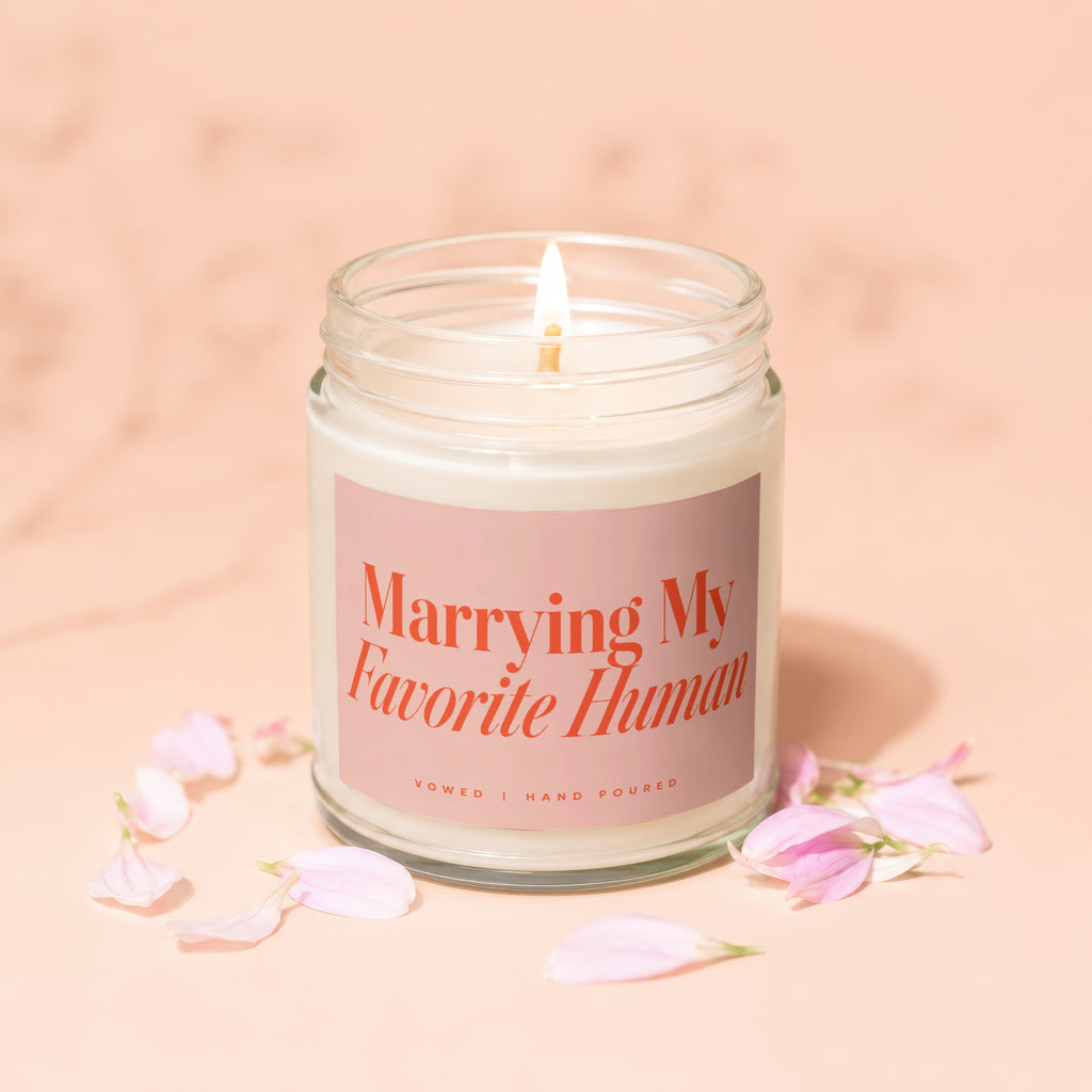 A lit candle with pink label saying "Marrying My Favorite Human" surrounded by petals.