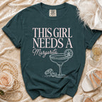 Teal t-shirt with pink text "THIS GIRL NEEDS A Margarita" and margarita graphic.