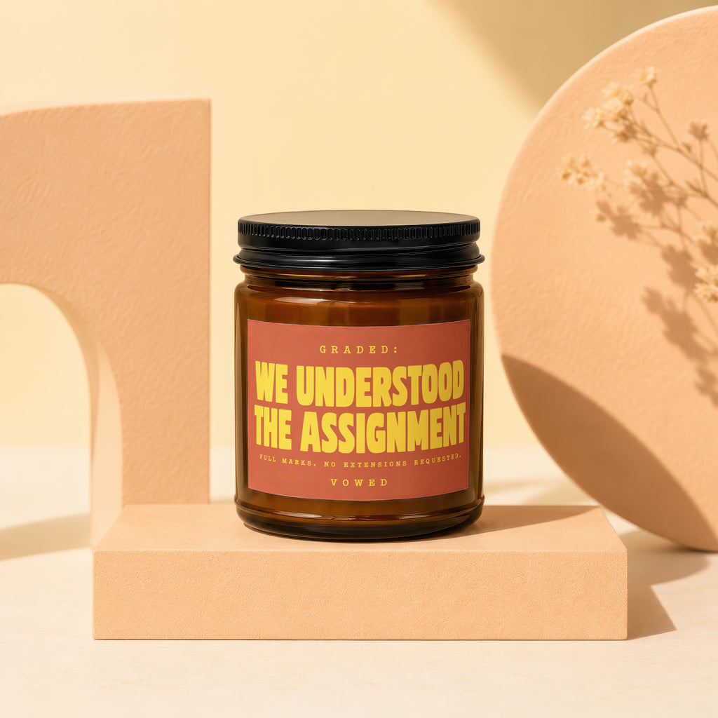 Amber jar candle with "We Understood the Assignment" text on label.