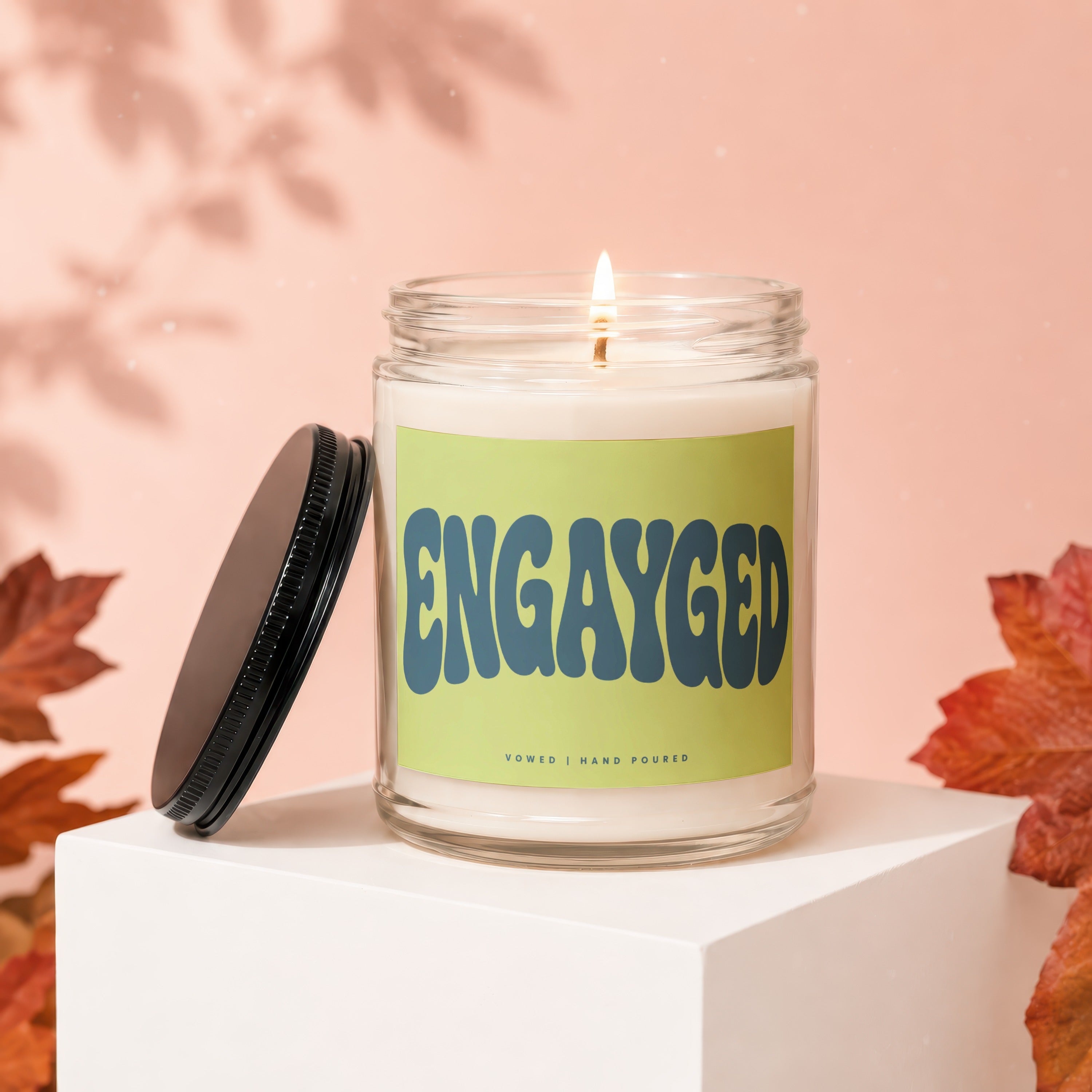 Glass candle with "ENGAYGED" text on a light green label above "VOWED | HAND POURED".
