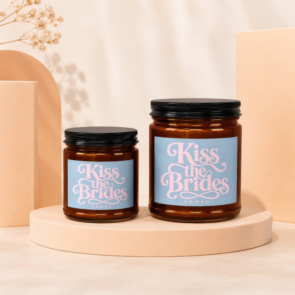 Two amber glass candles, labeled "Kiss the Brides Vowed," with black lids.
