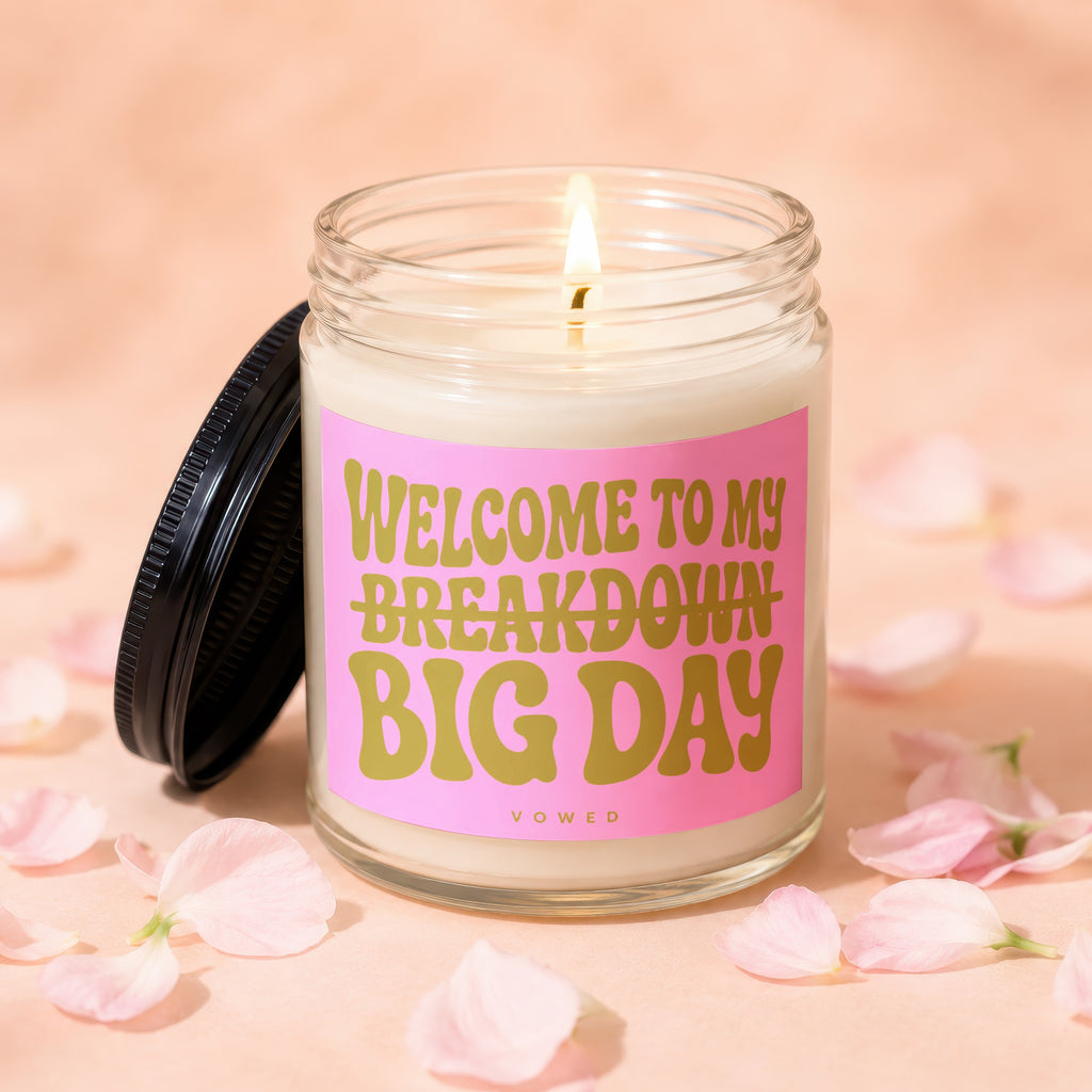 Candle with pink label reading "WELCOME TO MY BREAKDOWN BIG DAY" among petals.