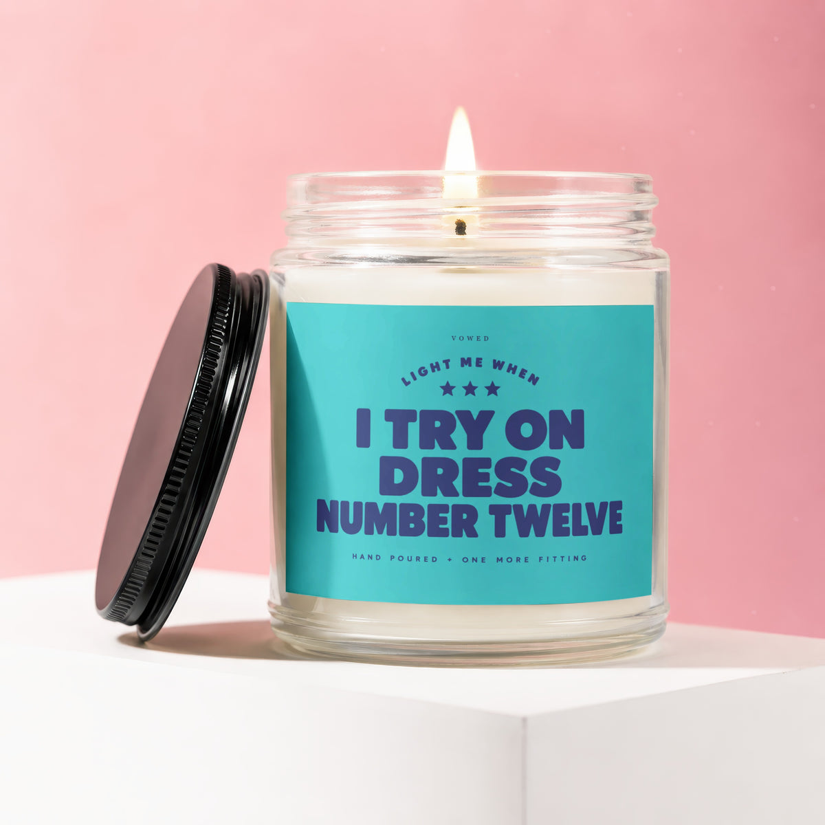 Lit candle with teal label reading "Light me when I try on dress number twelve."
