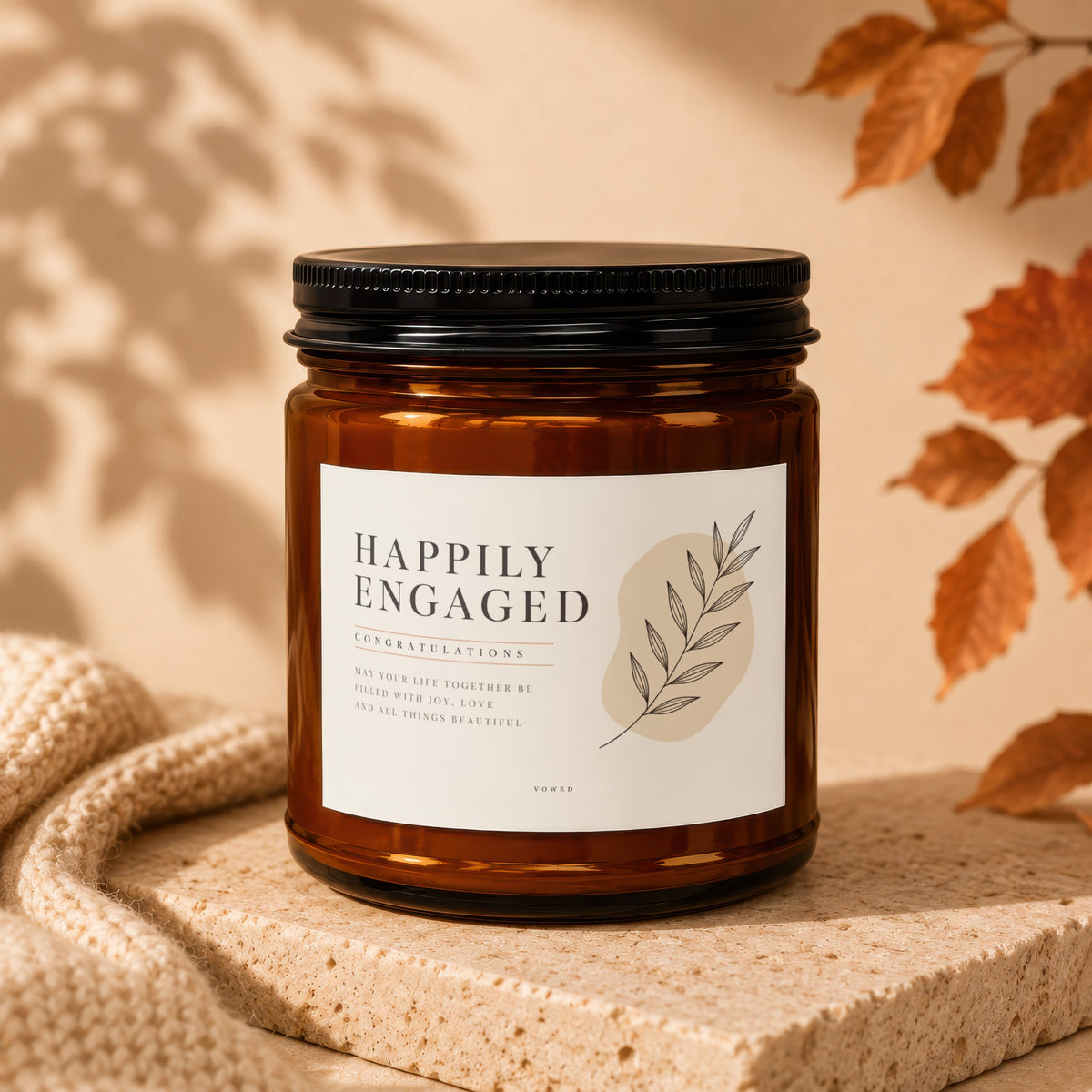 Amber glass candle with "Happily Engaged" label and botanical illustration.