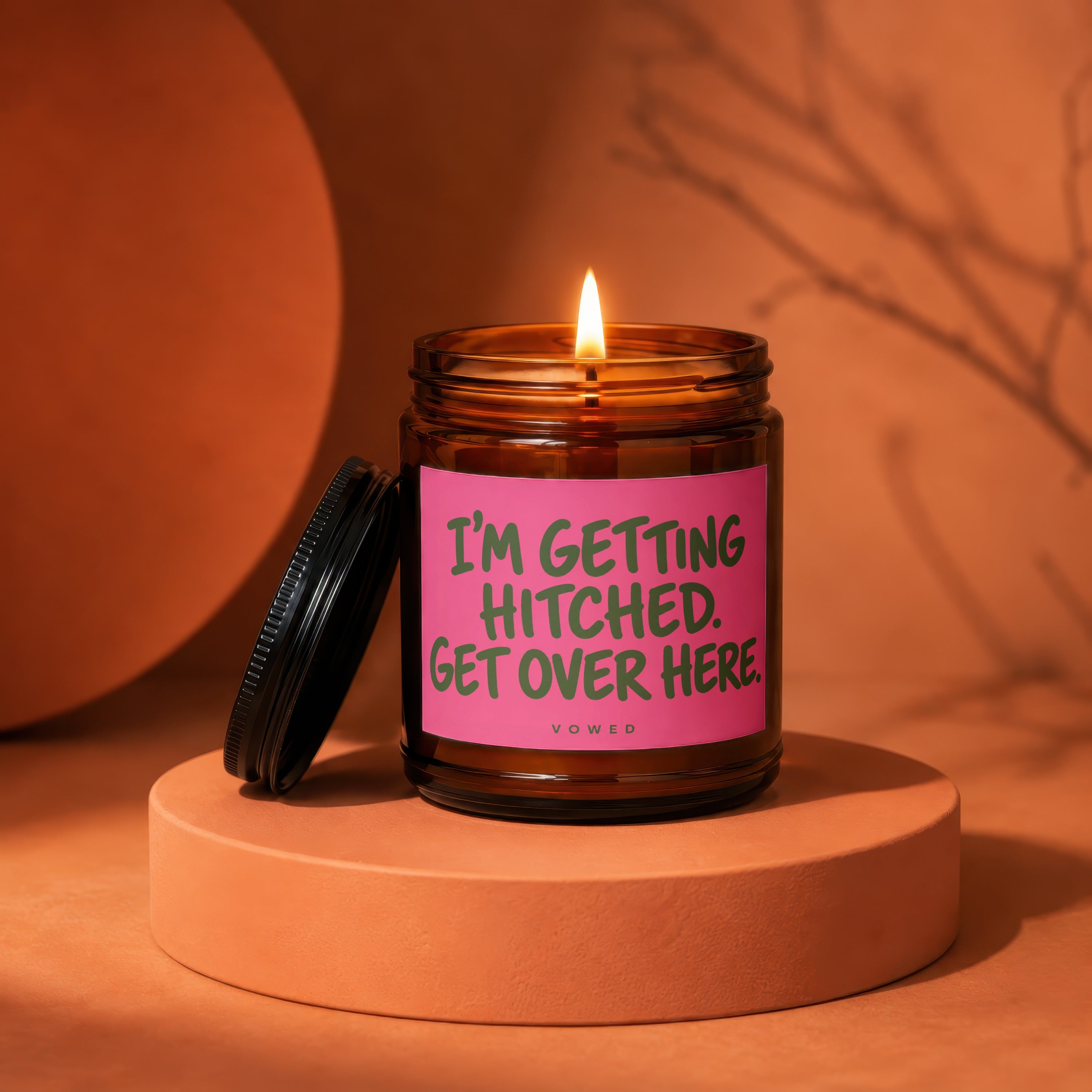 Brown glass candle with lit wick and pink label that reads "I'm getting hitched. Get over here."